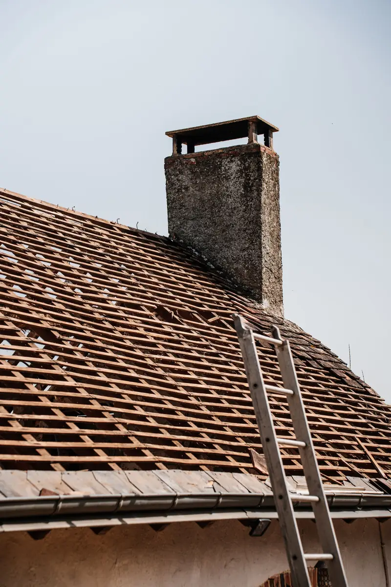 Oud pannendak met schouw en ladder, klaar voor renovatie