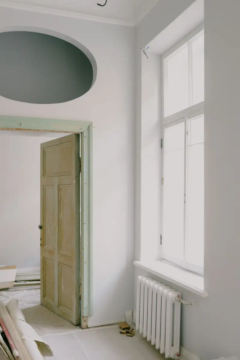Kamer in renovatie met hoog raam, radiator en een oude deur