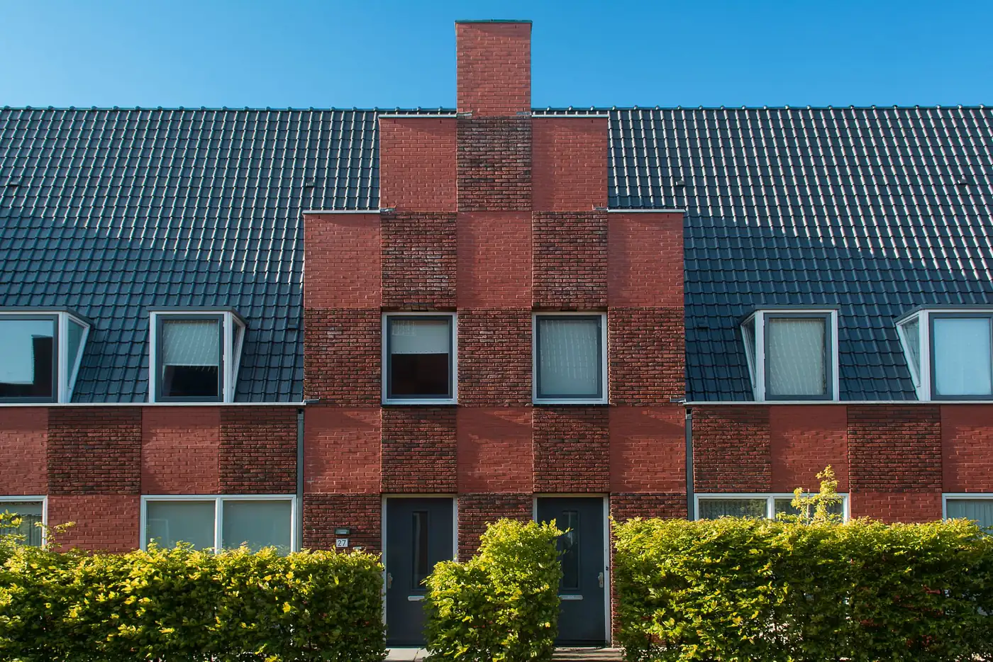 Rij bakstenen woningen met een trapgevel en lage hagen