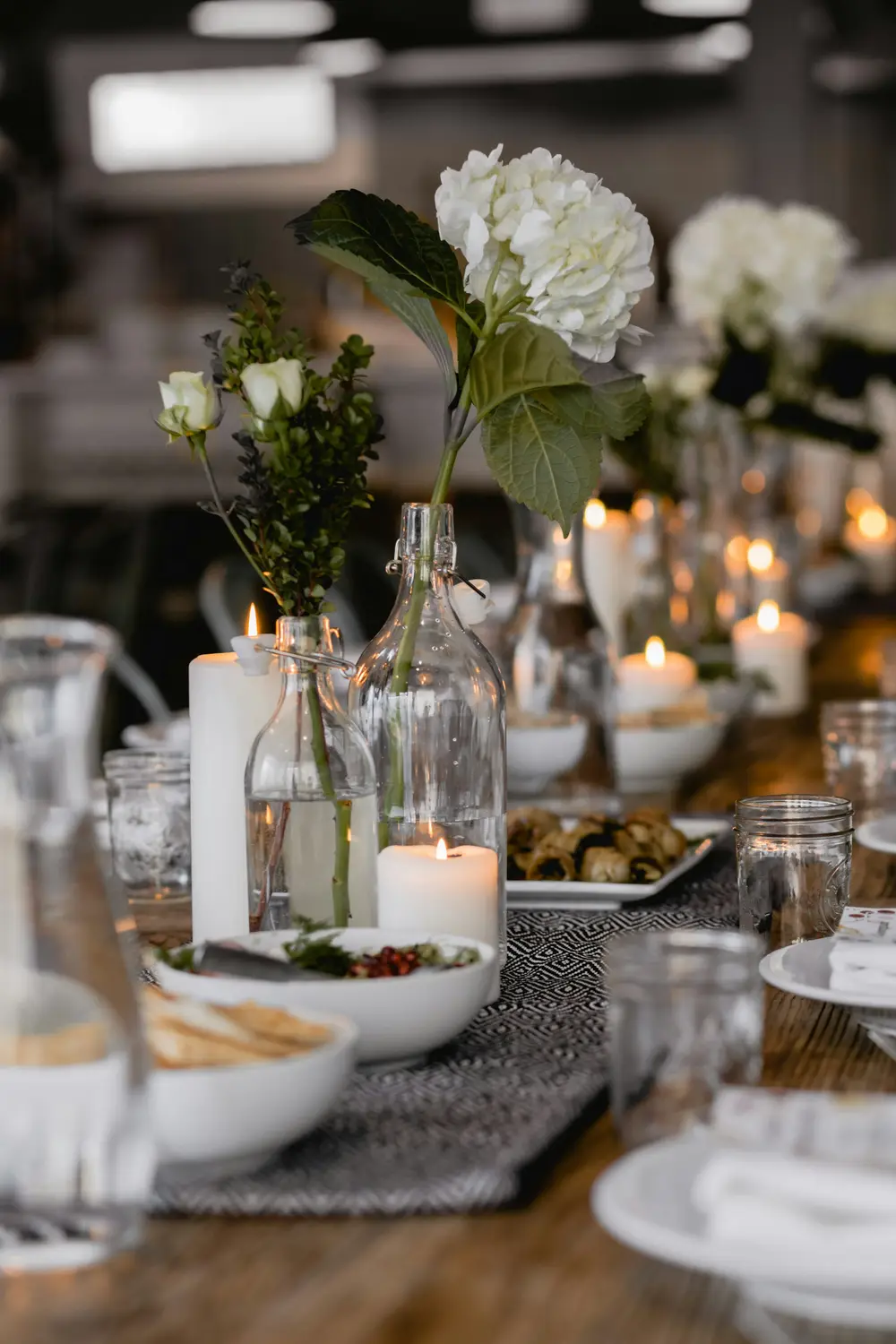 Witte bloemen in glazen flessen naast brandende kaarsen op tafel