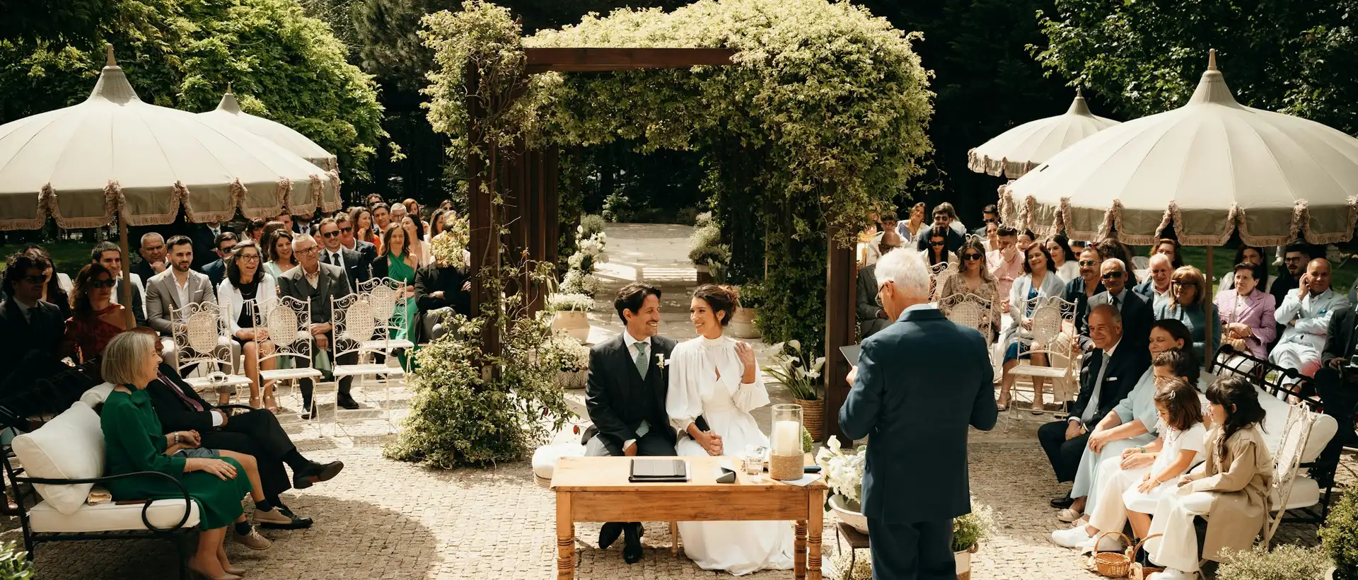 Een ceremonie in de tuin, met parasols, gasten en een boog vol groen
