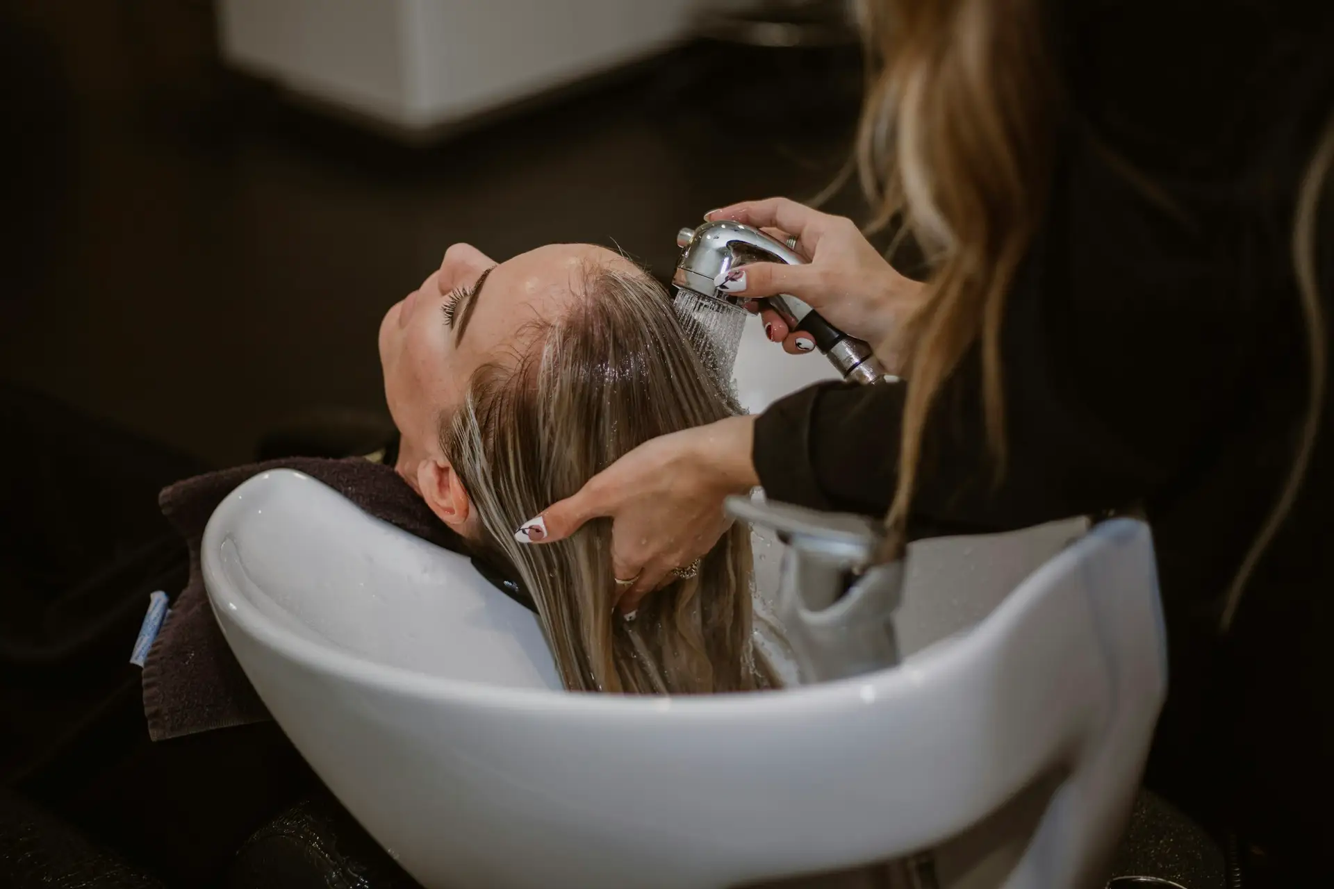 Een stylist wast het lange blonde haar van een klant aan de wasbak