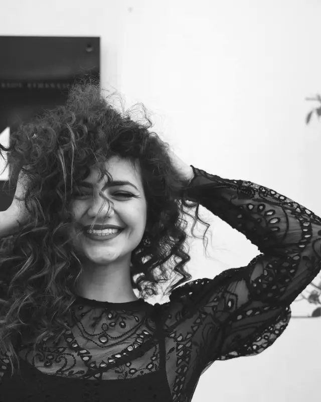 Portret van stylist Yasmine, lachend met haar handen in haar krullen