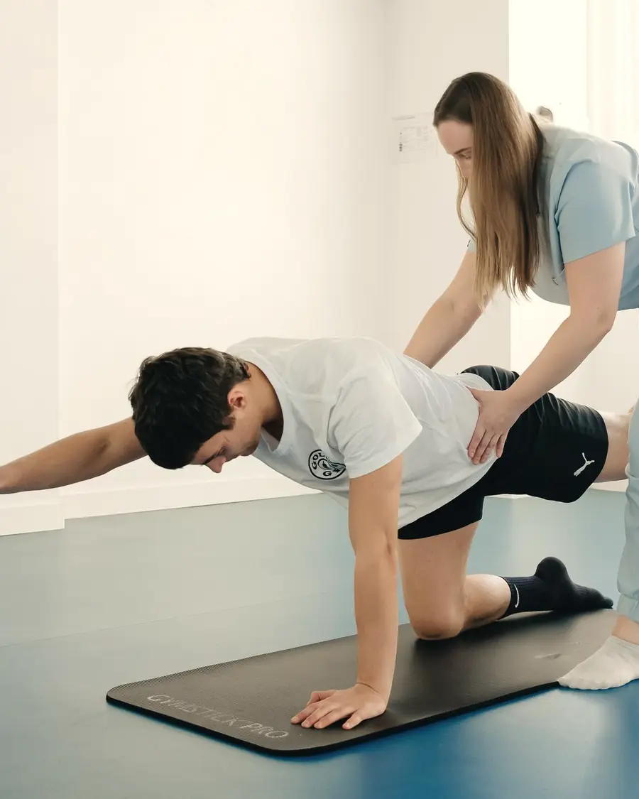 Een kinesist begeleidt een patiënt bij een oefening op de mat in de oefenzaal